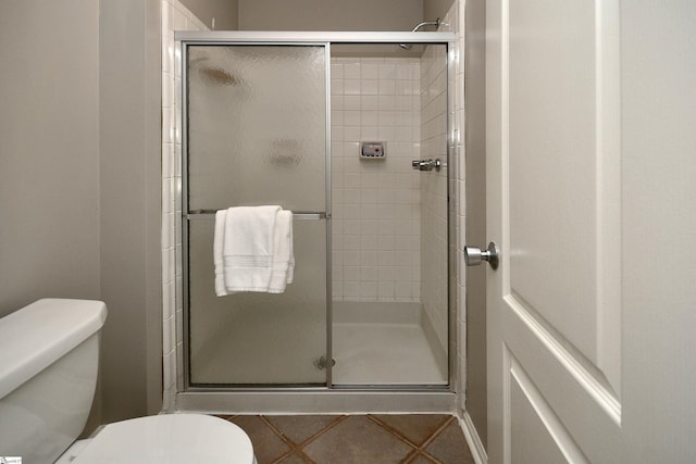 bathroom featuring a shower with door, tile patterned flooring, and toilet