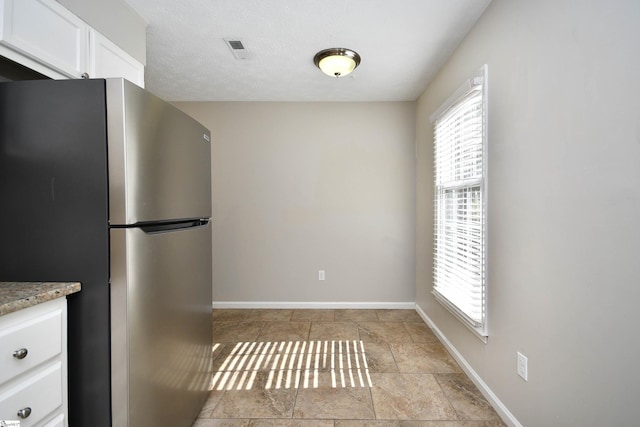 kitchen with stainless steel refrigerator, white cabinetry, and a textured ceiling