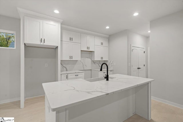 kitchen featuring white cabinets, light stone counters, sink, and a kitchen island with sink