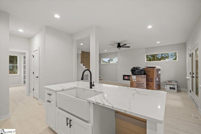 kitchen featuring light stone countertops, sink, a kitchen island with sink, and light wood-type flooring