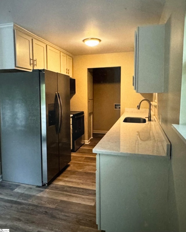 kitchen with stainless steel refrigerator with ice dispenser, light stone counters, dark wood-type flooring, and sink