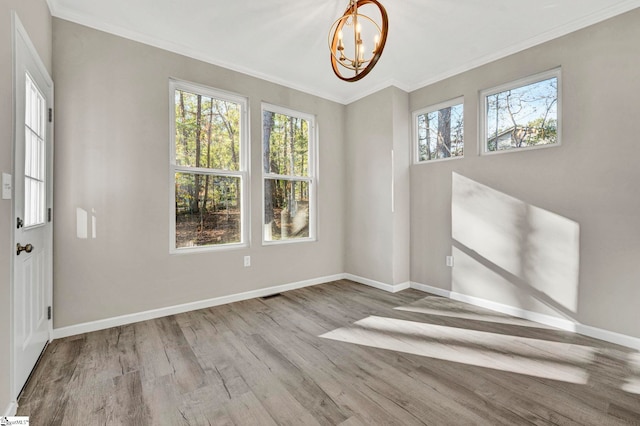 spare room with a notable chandelier, light wood-type flooring, and ornamental molding