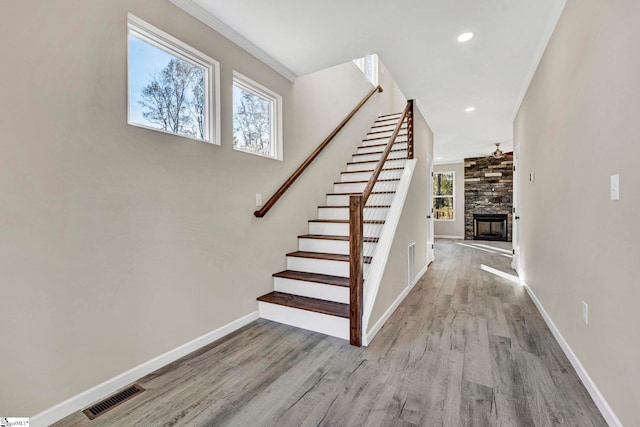 staircase featuring hardwood / wood-style floors, ceiling fan, a stone fireplace, and ornamental molding