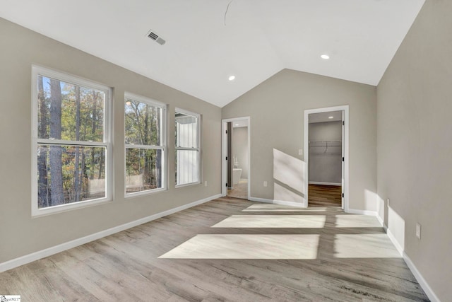 unfurnished bedroom featuring vaulted ceiling, ensuite bath, light hardwood / wood-style flooring, a spacious closet, and a closet