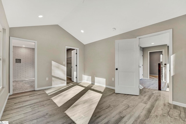 unfurnished bedroom featuring ensuite bathroom, light hardwood / wood-style flooring, and lofted ceiling