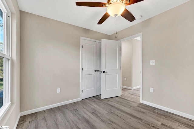 unfurnished bedroom featuring ceiling fan, a closet, light wood-type flooring, and multiple windows