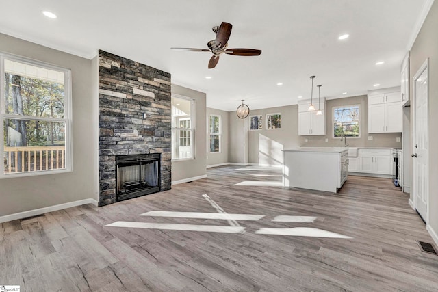 unfurnished living room with ceiling fan, a fireplace, light hardwood / wood-style floors, and ornamental molding