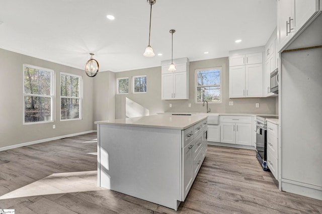 kitchen with hanging light fixtures, white cabinets, stainless steel appliances, and light wood-type flooring