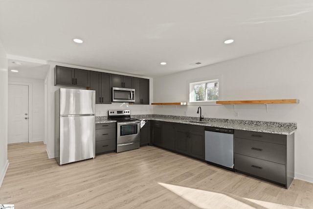 kitchen with stainless steel appliances, light stone counters, light hardwood / wood-style floors, and sink