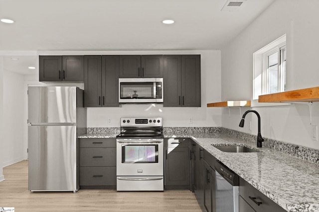 kitchen featuring light wood-type flooring, stainless steel appliances, light stone counters, and sink