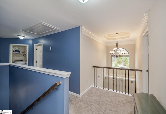 hall with a tray ceiling, ornamental molding, washer / clothes dryer, light colored carpet, and a chandelier