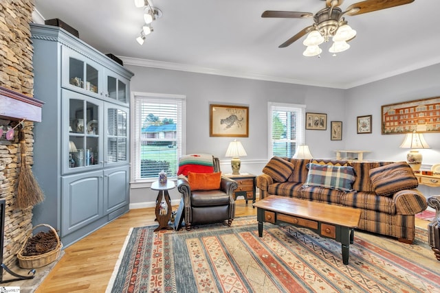 living room with ceiling fan, rail lighting, light wood-type flooring, a fireplace, and ornamental molding