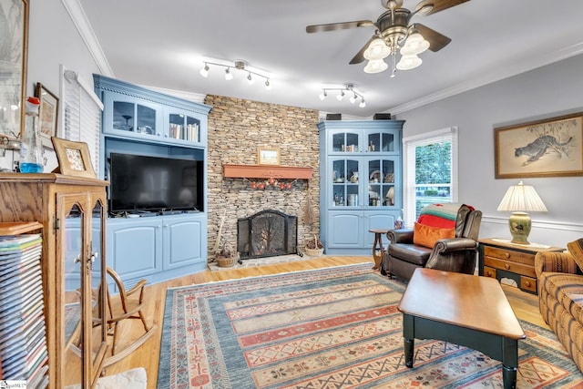 living room featuring ceiling fan, light hardwood / wood-style floors, a stone fireplace, and crown molding