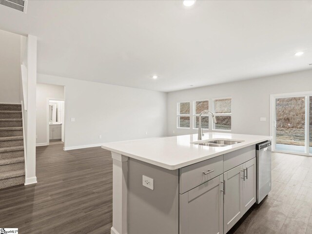 kitchen with sink, dark wood-type flooring, gray cabinetry, an island with sink, and stainless steel dishwasher