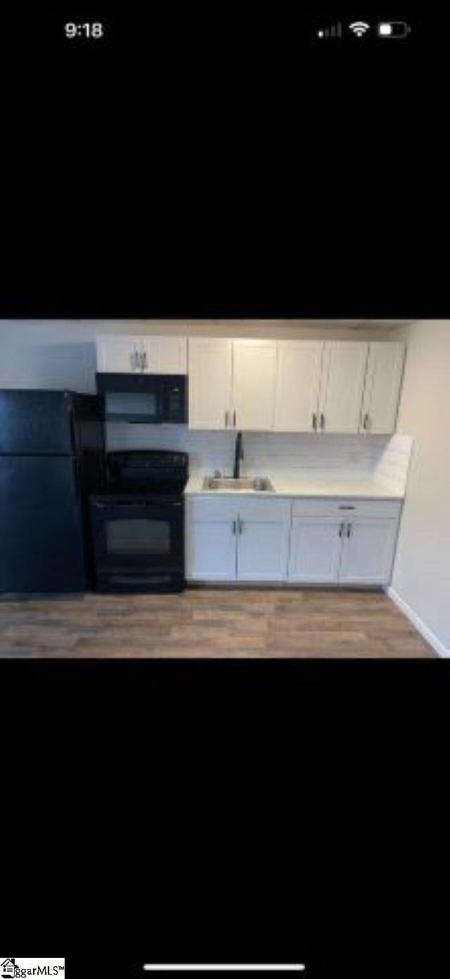 kitchen featuring white cabinets, sink, black appliances, and light hardwood / wood-style flooring