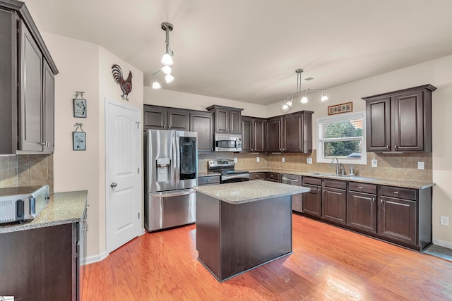 kitchen featuring appliances with stainless steel finishes, light hardwood / wood-style floors, a kitchen island, and hanging light fixtures