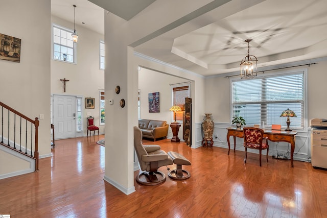 foyer entrance featuring a raised ceiling, light wood-type flooring, an inviting chandelier, and crown molding