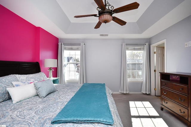 carpeted bedroom with a tray ceiling, multiple windows, and ceiling fan