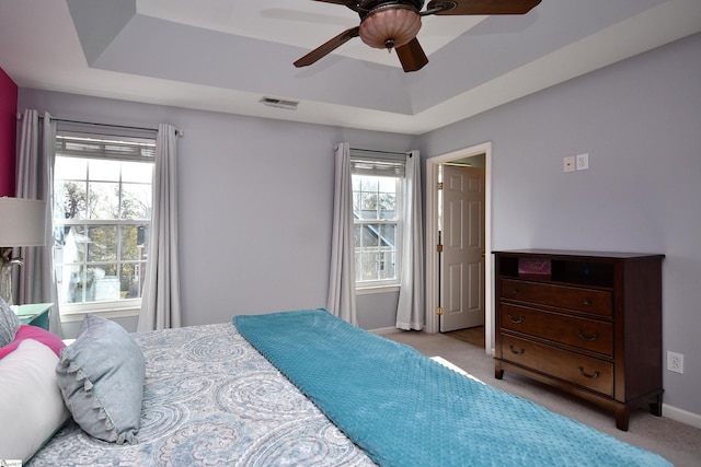 bedroom with ceiling fan, light carpet, and a tray ceiling