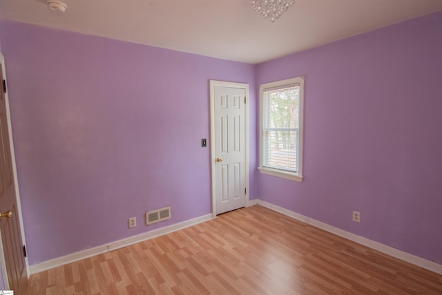 empty room featuring light wood-type flooring and an inviting chandelier