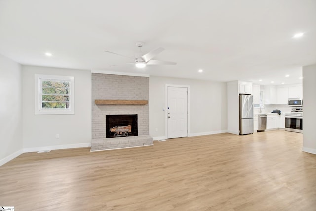 unfurnished living room with a fireplace, light hardwood / wood-style flooring, ceiling fan, and sink