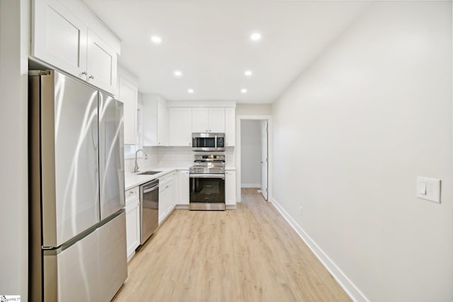 kitchen with sink, light hardwood / wood-style flooring, decorative backsplash, white cabinetry, and stainless steel appliances