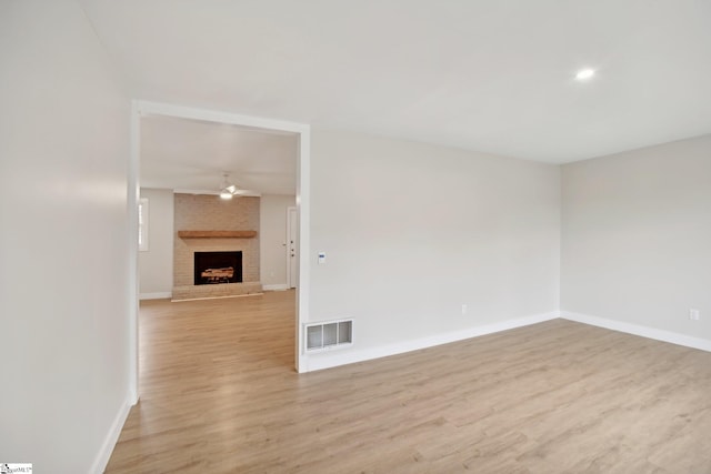 spare room featuring ceiling fan, light wood-type flooring, and a fireplace