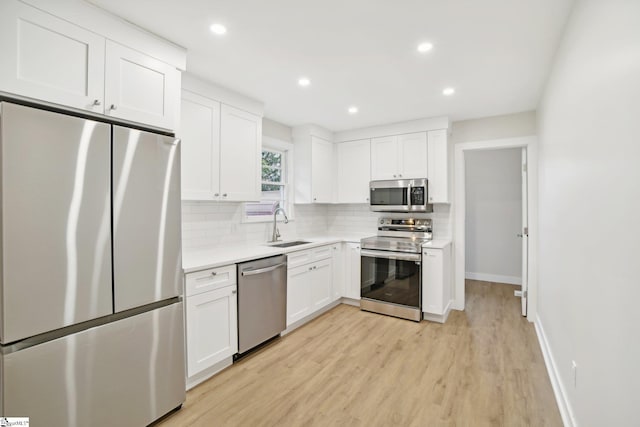 kitchen with decorative backsplash, appliances with stainless steel finishes, sink, white cabinets, and light hardwood / wood-style floors