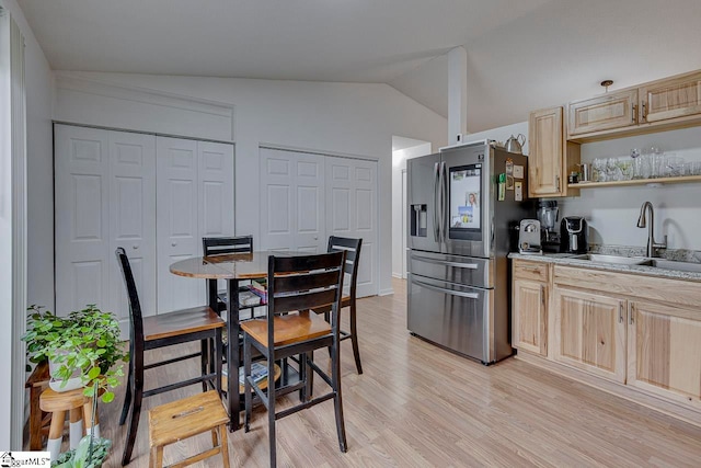 kitchen with sink, stainless steel refrigerator with ice dispenser, light brown cabinetry, and vaulted ceiling