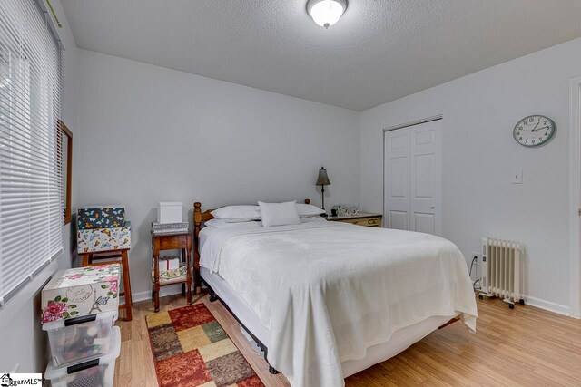 bedroom with a closet, radiator heating unit, a textured ceiling, and light wood-type flooring