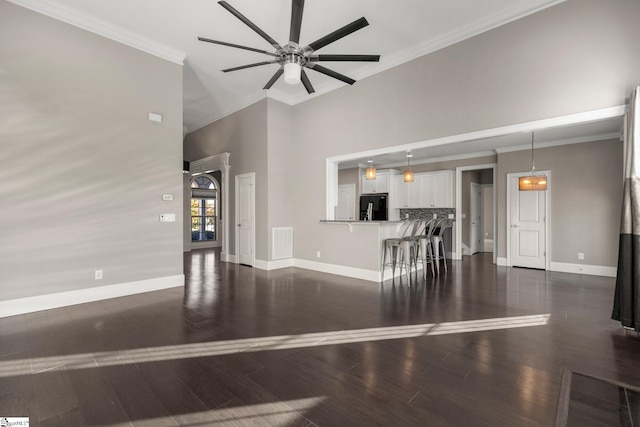 unfurnished living room featuring a towering ceiling, dark hardwood / wood-style floors, ceiling fan, and crown molding