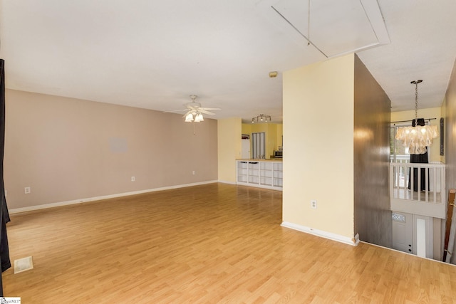 unfurnished living room with ceiling fan with notable chandelier and light hardwood / wood-style flooring