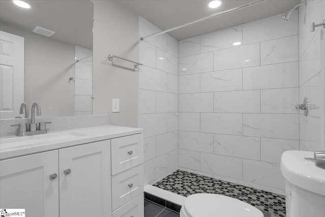 bathroom featuring tile patterned flooring, a tile shower, vanity, and toilet