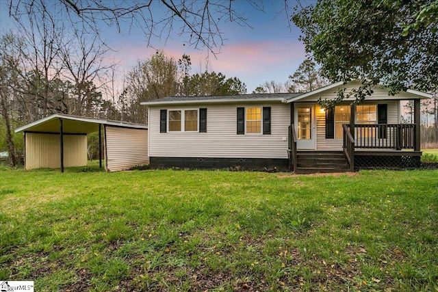 back house at dusk with covered porch, a carport, and a lawn