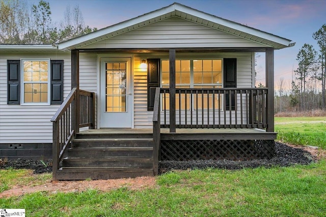 back house at dusk with covered porch and a yard