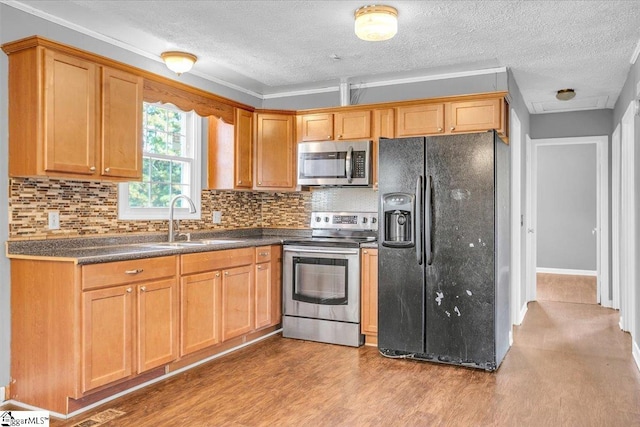 kitchen with sink, backsplash, a textured ceiling, appliances with stainless steel finishes, and light wood-type flooring