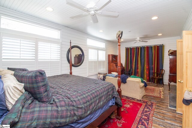 bedroom featuring dark hardwood / wood-style floors, ceiling fan, wooden walls, and multiple windows