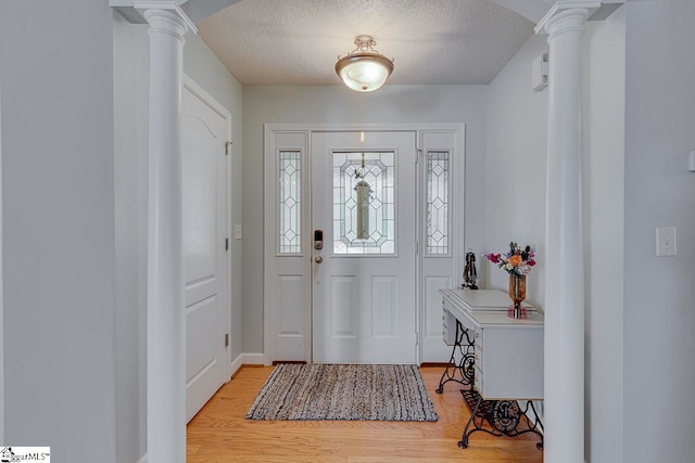 entrance foyer featuring ornate columns, light hardwood / wood-style flooring, and a textured ceiling