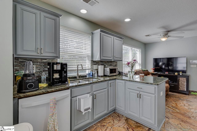 kitchen with kitchen peninsula, ceiling fan, sink, dark stone countertops, and dishwasher