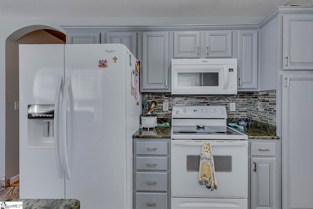 kitchen featuring decorative backsplash, gray cabinets, white appliances, and dark stone counters