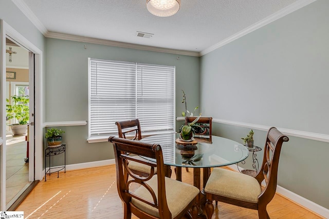 dining room with light hardwood / wood-style floors, a textured ceiling, and ornamental molding