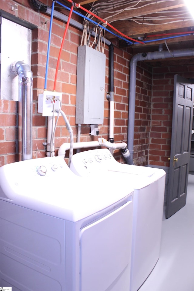 laundry area featuring electric panel, washer and dryer, and brick wall