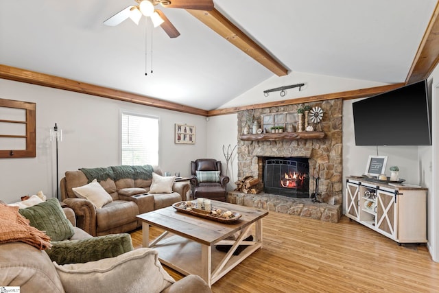 living room featuring vaulted ceiling with beams, light hardwood / wood-style floors, a stone fireplace, and ceiling fan