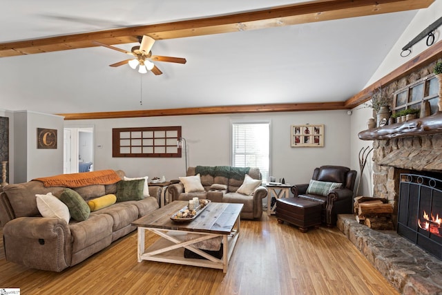 living room with lofted ceiling with beams, light hardwood / wood-style flooring, ceiling fan, and a stone fireplace