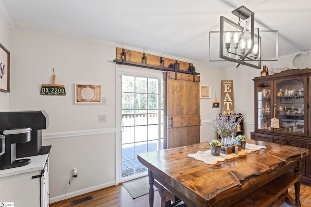 dining room with hardwood / wood-style flooring, a barn door, crown molding, and a chandelier