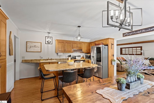 kitchen with a notable chandelier, pendant lighting, light wood-type flooring, appliances with stainless steel finishes, and ornamental molding