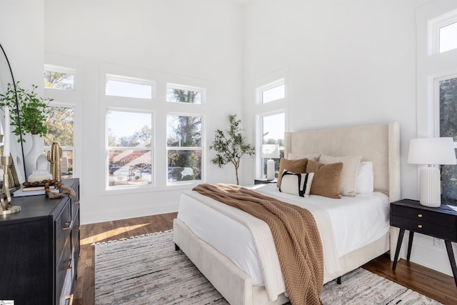 bedroom with multiple windows, wood-type flooring, and a high ceiling