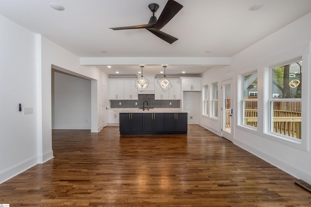 kitchen with white cabinets, dark hardwood / wood-style flooring, decorative light fixtures, and an island with sink