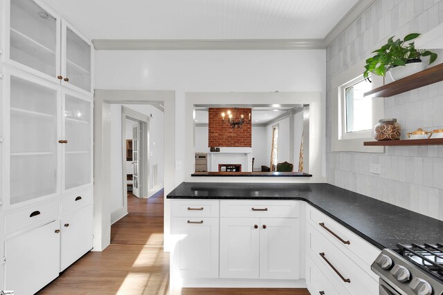 kitchen with white cabinets, light hardwood / wood-style floors, backsplash, crown molding, and stainless steel range with gas stovetop