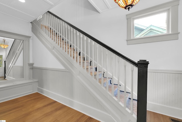 staircase with wood-type flooring and an inviting chandelier